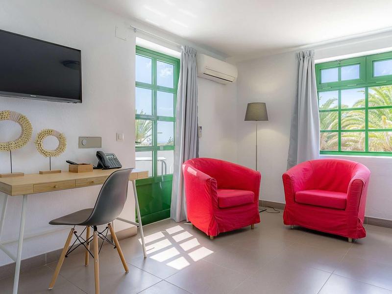 Heller Raum mit roten Sesseln, grünem Fenster, Schreibtisch und Stuhl in modernem Stil.