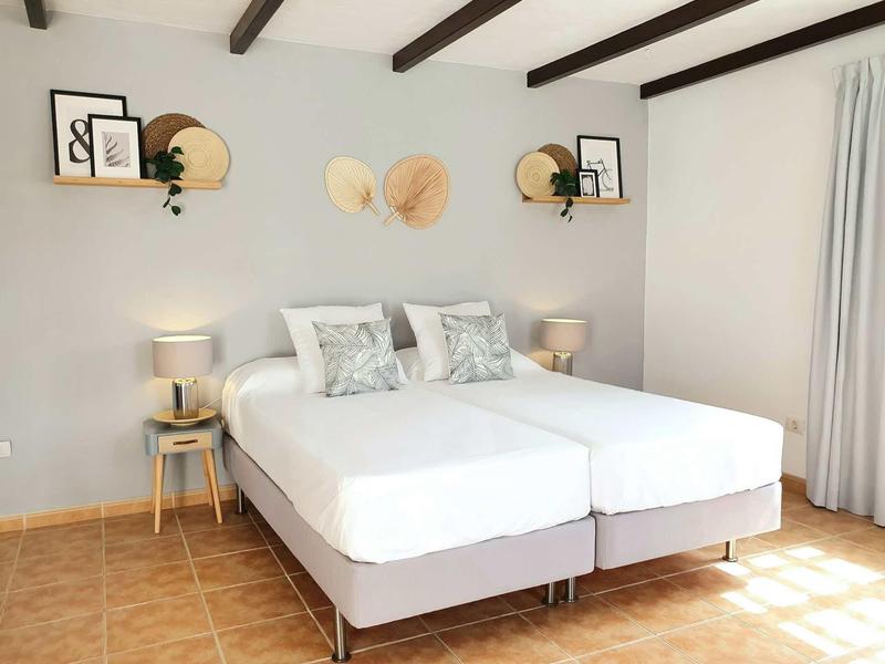 Helles Schlafzimmer mit zwei Einzelbetten, Holzregalen, Deko und warmem Licht.