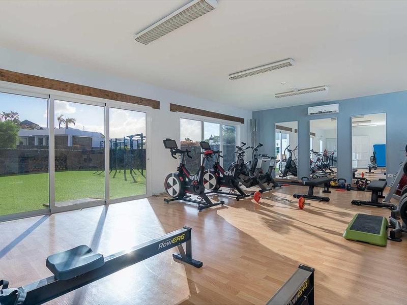 Heller Fitnessraum mit großen Fenstern, Holzboden und verschiedenen Trainingsgeräten.