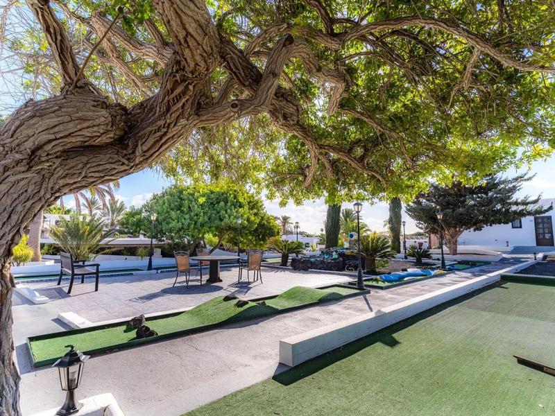 Freizeitpark mit Minigolfbahn, Bäumen und weiß getünchten Gebäuden unter klarem Himmel.