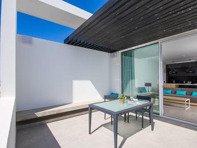 Moderner Balkon mit weißer Wand, grauem Tisch, zwei Stühlen und direktem Zugang zum Wohnzimmer.