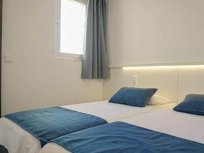 Ein schlicht eingerichtetes Schlafzimmer mit zwei Einzelbetten, blauen Decken und Kissen, weißer Wand.