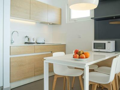 Moderne kleine Küche mit Holzmöbeln, weißem Tisch, Stühlen und Obstschale auf dem Tisch.