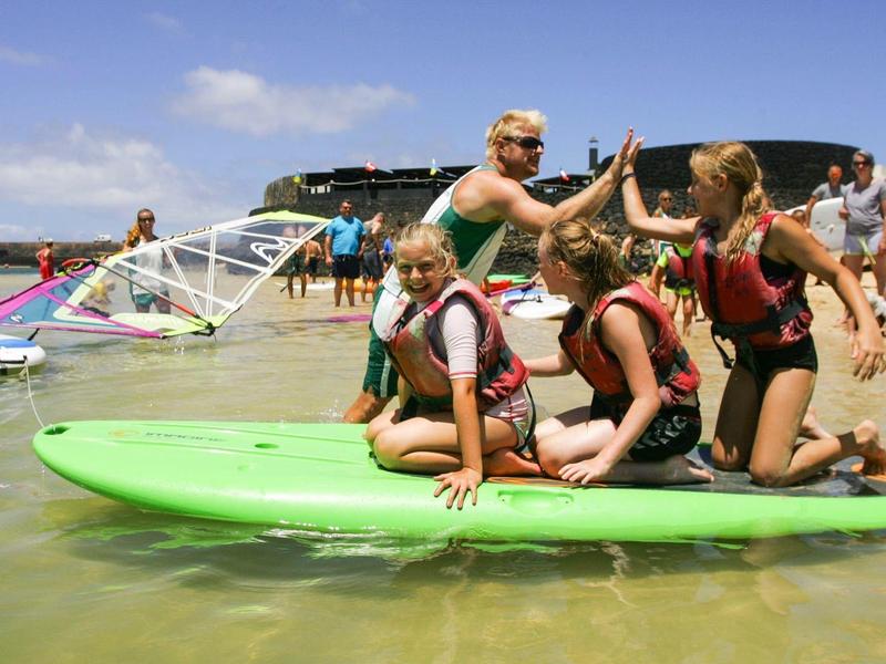 Group of people wearing life jackets on a green paddleboard in shallow water.