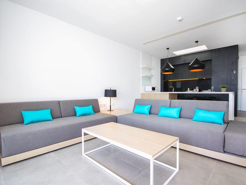 Modern living room with gray sofas, blue cushions, and a minimalist kitchen in the background.