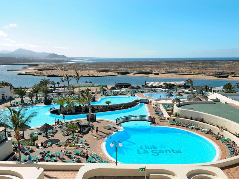 View of a resort with multiple blue pools, sun loungers, and a calm sea in the background.