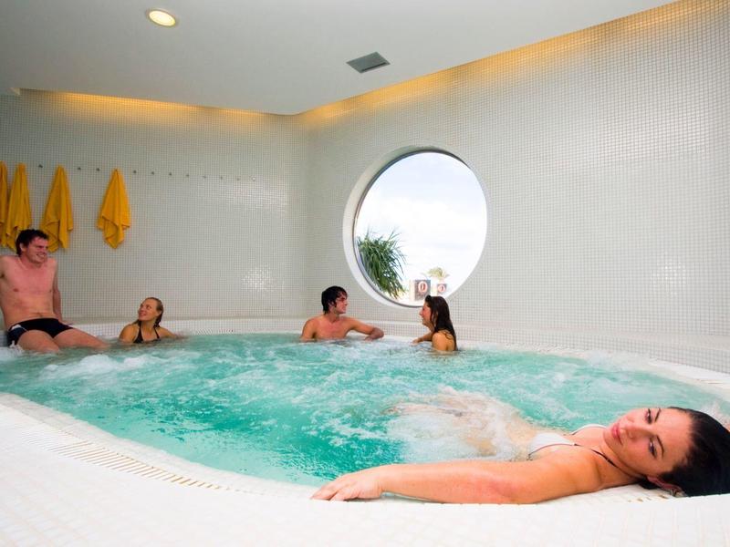 People relax in a hot tub in a modern, bright room with a round window.