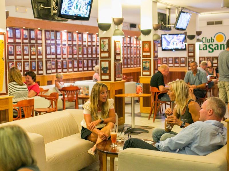 Guests relax in a cozy hotel lounge with bright sofas and televisions.