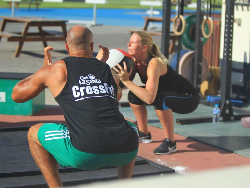Two people are exercising together with weights outdoors at a CrossFit gym.