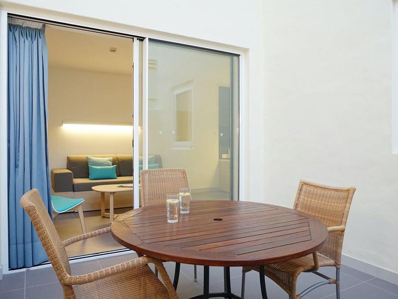 Round wooden table with two chairs on a terrace in front of a glass sliding door to the living room.