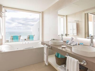 Modernes Badezimmer mit großer Badewanne, Doppelwaschbecken und Blick auf Meer und Balkon.