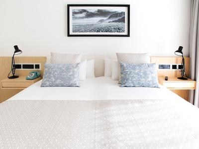 Modernes Hotelzimmer mit großem Doppelbett und Nachttischen mit Lampen.