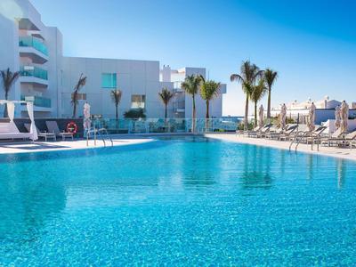 Großer, klarer Pool mit Liegestühlen und Palmen an sonnigem, blauem Himmel in moderner Anlage.