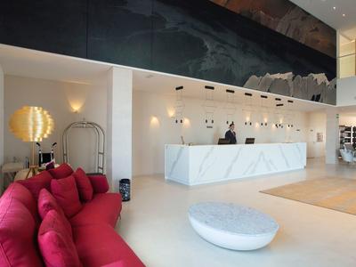 Moderne Hotellobby mit weißem Empfangstresen, rotem Sofa und rundem weißen Hocker.