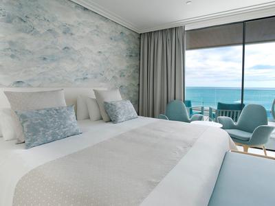 Helles Schlafzimmer mit großem Bett, weichen Kissen und Meerblick durch bodentiefe Fenster.