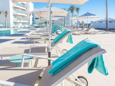 Poolbereich mit Liegestühlen und türkisfarbenen Handtüchern unter Sonnenschirmen bei klarem Himmel.