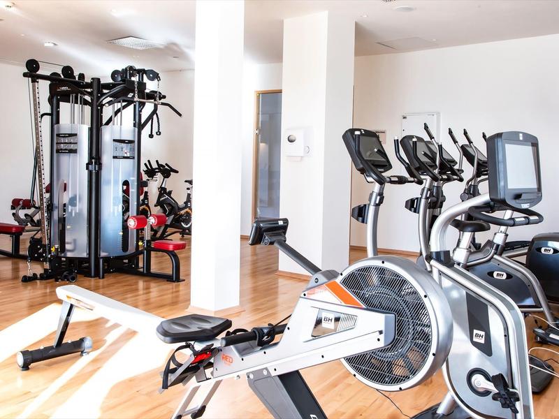 Fitnessraum mit Rudergerät, Ergometer und Mehrstationstrainer in hellem, modernem Raum.