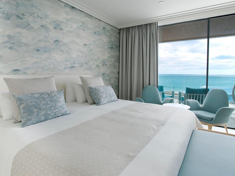 Helles Schlafzimmer mit großem Bett, weichen Kissen und Meerblick durch bodentiefe Fenster.