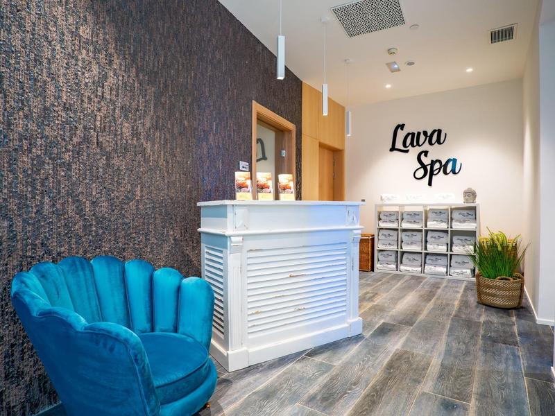 Moderner Spa-Empfang mit weißem Tresen, blauem Samtsessel und Holzoptik-Bodenbelag.