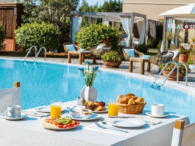 Ein gedeckter Tisch mit Frühstück am Pool, umgeben von Stühlen und Pavillons im Garten.