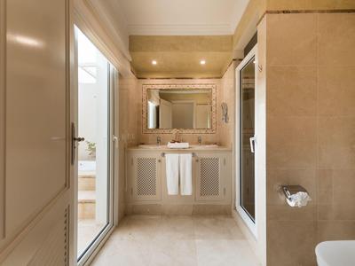 Moderner, heller Badezimmerbereich mit Waschtisch, Spiegel, Glasdusche und beigem Fliesenboden.