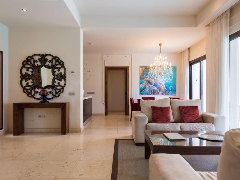 Heller Wohnbereich mit beiger Couch, Glas-Couchtisch, großem Spiegel und farbenfrohem Gemälde.