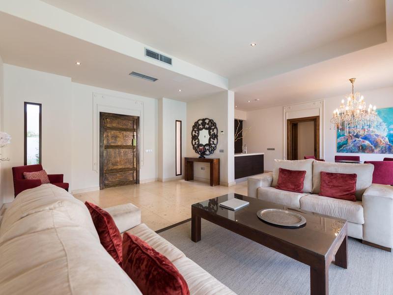 Heller Wohnraum mit weißen Sofas, roten Kissen, dunklem Tisch und modernem Kunstwerk an Wand.