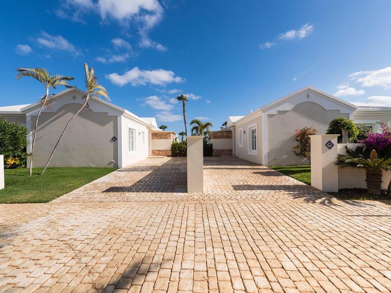 Zwei weiße Häuser mit roten Dächern und Palmen auf gepflastertem Hof bei blauem Himmel.