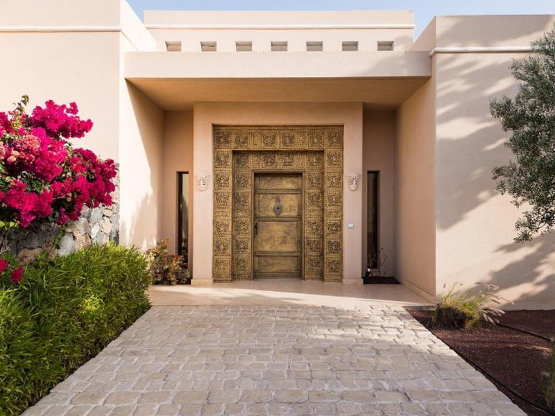 Moderner Hauseingang mit großen, dekorativen Holztüren, umgeben von weißen Wänden und grünen Pflanzen.