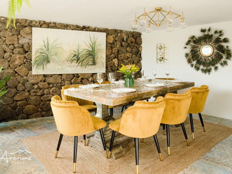 Hell eingerichteter Essbereich mit gelben Stühlen, Holztisch, Steinwand und Pflanzen an der Wand.