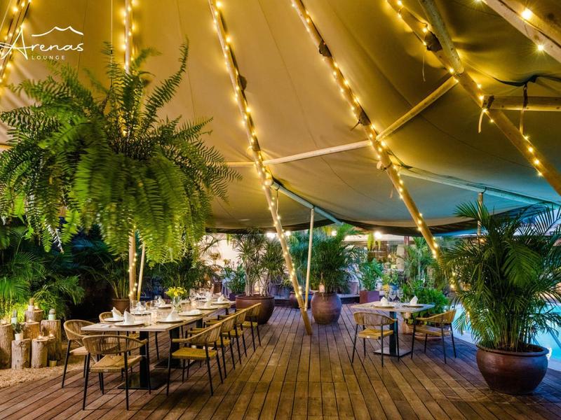 Gemütliche Außengastronomie mit Holzboden, Pflanzen und warmen Lichterketten unter Zelt.