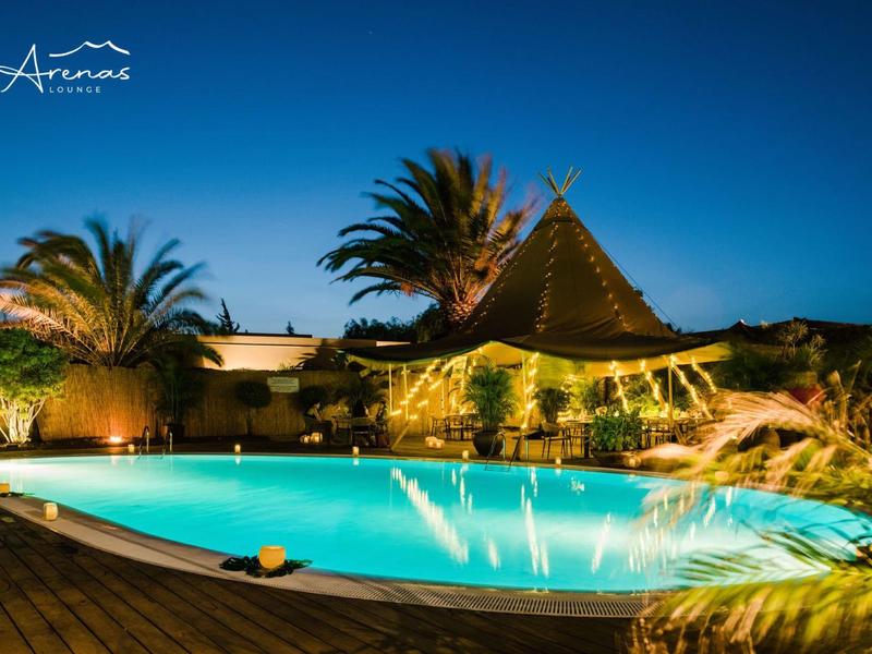 Beleuchteter Pool mit Palmen und exotischem Gebäude bei Abenddämmerung in tropischer Umgebung.