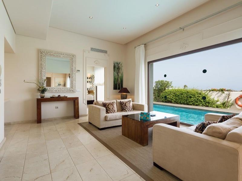 Modernes Wohnzimmer mit beiger Einrichtung, großen Fenstern und Blick auf Pool und Garten.