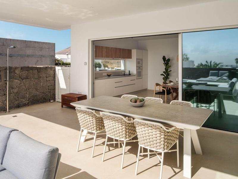 Moderne Terrasse mit großem Esstisch, sechs Stühlen, Sofas und Blick durch Glas-Schiebetür ins Innere.