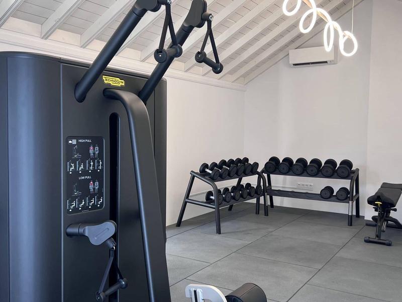 Moderner Fitnessraum mit Kraftmaschine, Hanteln auf Ablage und hellem Raum mit hohen Decken.