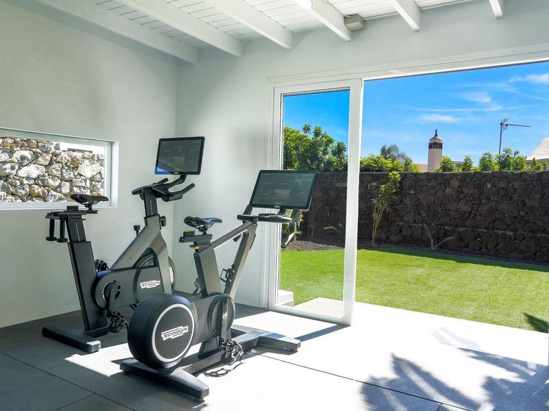 Helles Fitnesszimmer mit zwei Fahrradergometern, großem Fenster und Blick auf grünen Garten.