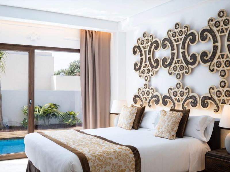 Hell eingerichtetes Schlafzimmer mit großem Bett, dekorativen Kissen und Muster an der Wand.