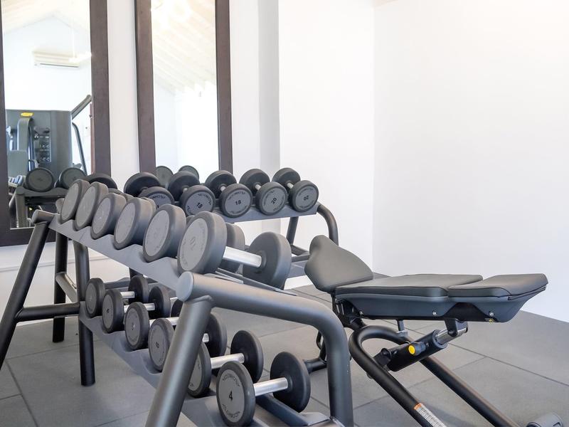 Helles Fitnessstudio mit verschiedenen Kurzhanteln und verstellbarer Trainingsbank in Grau.