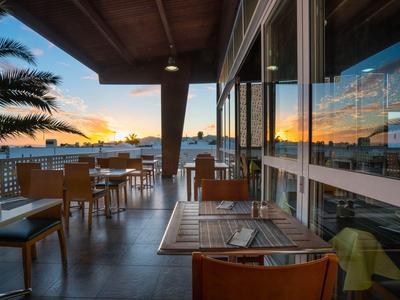 Terrasse d'hôtel avec tables et chaises au coucher du soleil avec des palmiers
