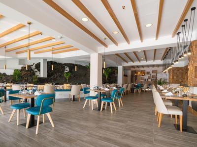 Heller, moderner Gastraum mit Holzbalkendecke, blauen Stühlen und weißen Tischen.