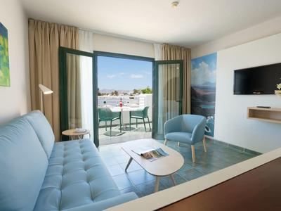 Hell eingerichtetes Wohnzimmer mit hellblauem Sofa, Sesseln und offener Balkontür mit Stadtblick.