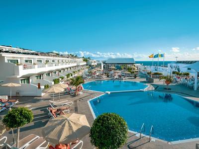 Grand piscine d'hôtel avec parasols et chaises longues, vue sur la mer par ciel dégagé.