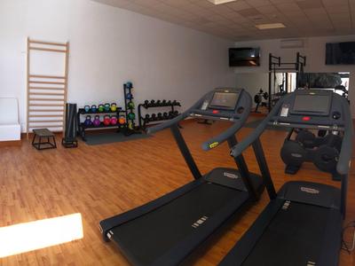 Salle de sport moderne avec tapis roulants, haltères et équipements d'exercice sur un sol en bois.