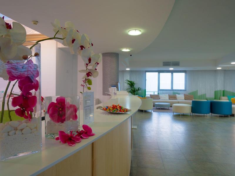 Heller Wartebereich mit weißen Sofas, bunten Poufs und Dekoration aus Orchideen auf Theke.