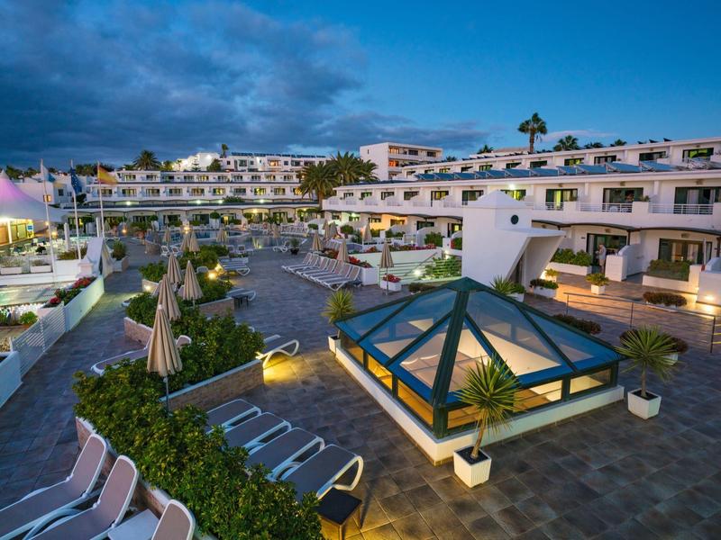 Blick auf moderne, weiße Hotelanlage mit Pool und Liegestühlen bei Abenddämmerung.