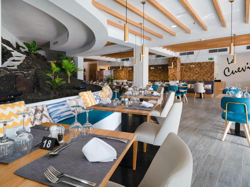 Modernes Restaurant mit weißen Stühlen, blauen Hockern, Holzdecke und dekorativem Fels im Innenraum.