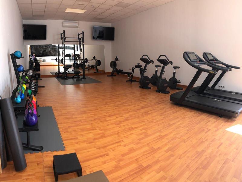 Ein heller Fitnessraum mit Laufbändern, Fahrrädern, Hanteln und Trainingsmatten auf Holzfußboden.