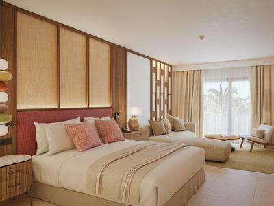Modernes Hotelzimmer mit großem Bett, Sesseln und warmen Holz- und Beigetönen.