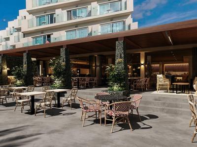 Außenbereich eines Hotels mit Tischen und Stühlen unter einem überdachten Bereich bei klarem Himmel.