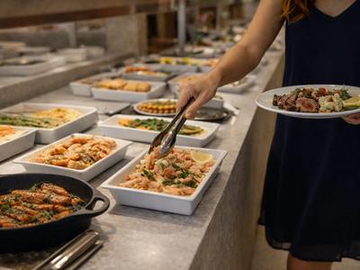 Person nimmt Essen von einem Buffet mit verschiedenen warmen Gerichten in Schalen.